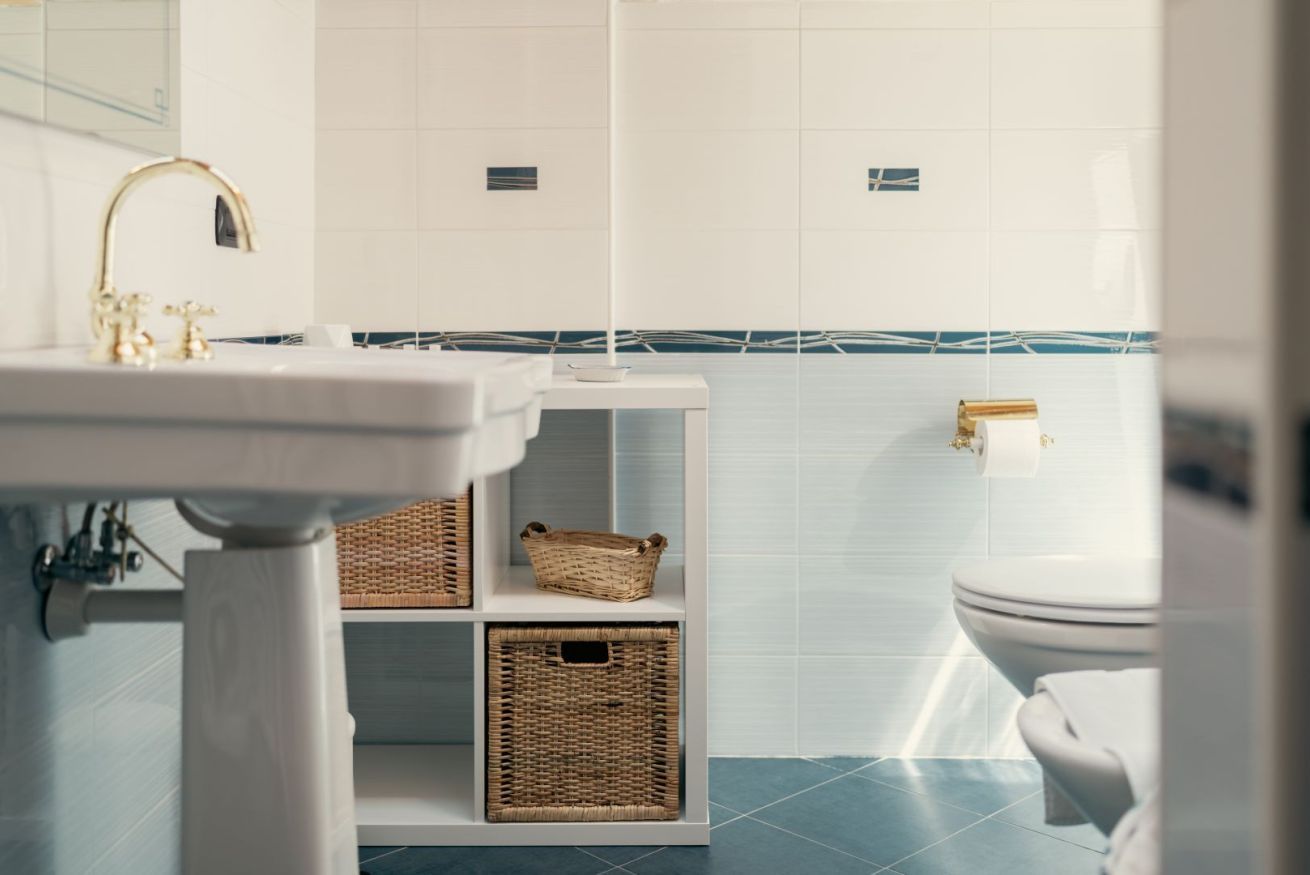 Ein Badezimmer mit einem weißen Waschbecken, einer Toilette und Körben aus Weidwerk auf Regalen.