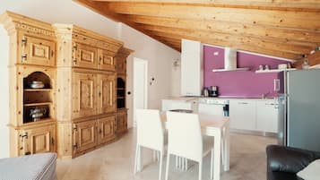 Una cuina moderna amb armaris de fusta, una zona de menjador amb caires blancs i una paret de color morat.