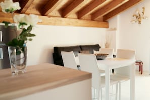 A dining area with a white table and chairs, a vase with white flowers, and a black sofa in the background.