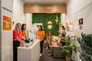 Un espace d’accueil avec une enseigne en bois au-dessus du comptoir, un mur vert agrémenté d’un luminaire suspendu et un bureau d’accueil orné d’une plante en pot.