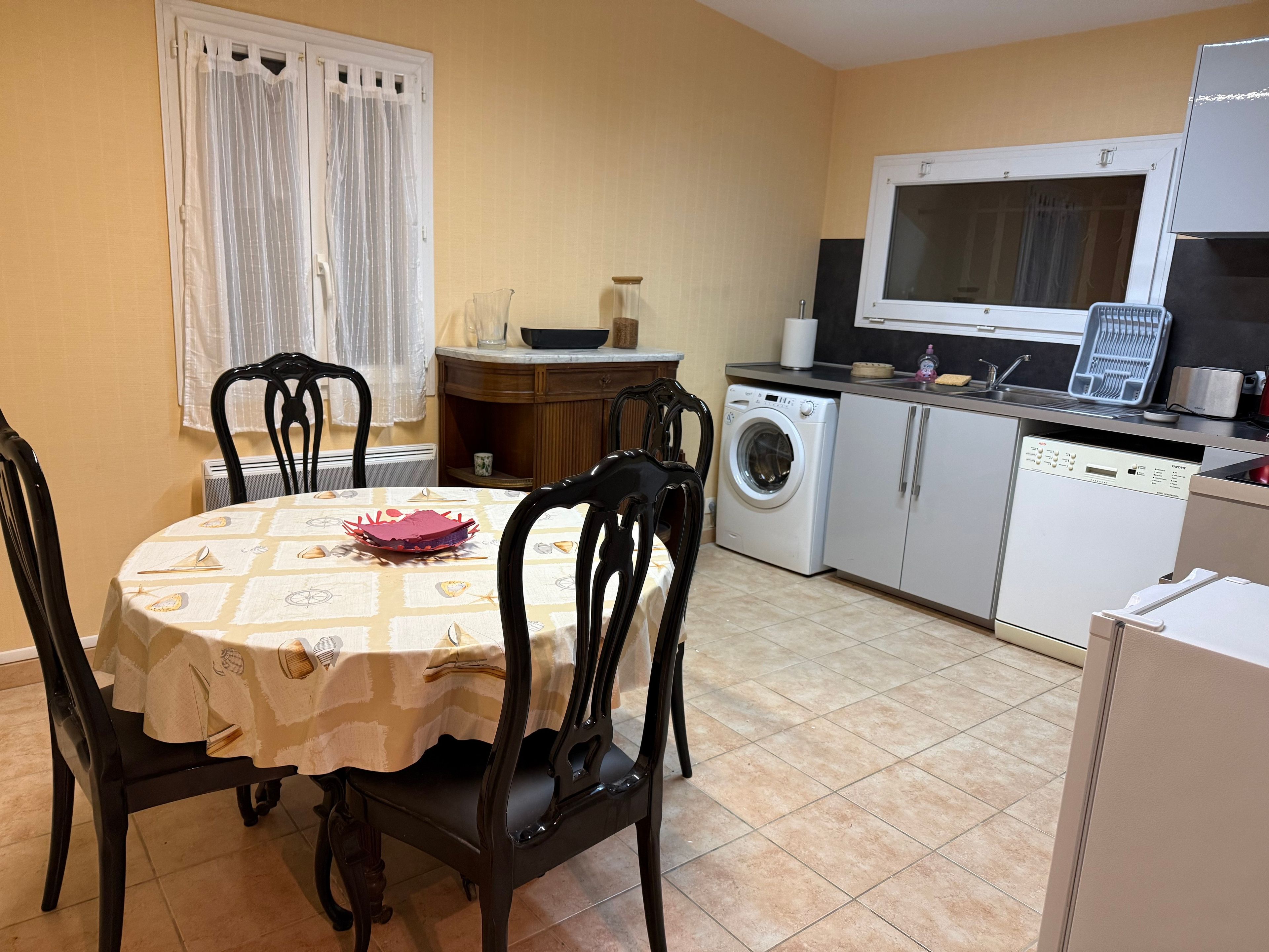 Una cocina compacta con lavadora, una mesa de comedor con sillas y una ventana con cortinas.