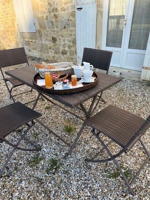 Un área de estar al aire libre con sillas de mimbre y una mesa dispuesta con alimentos para el desayuno.