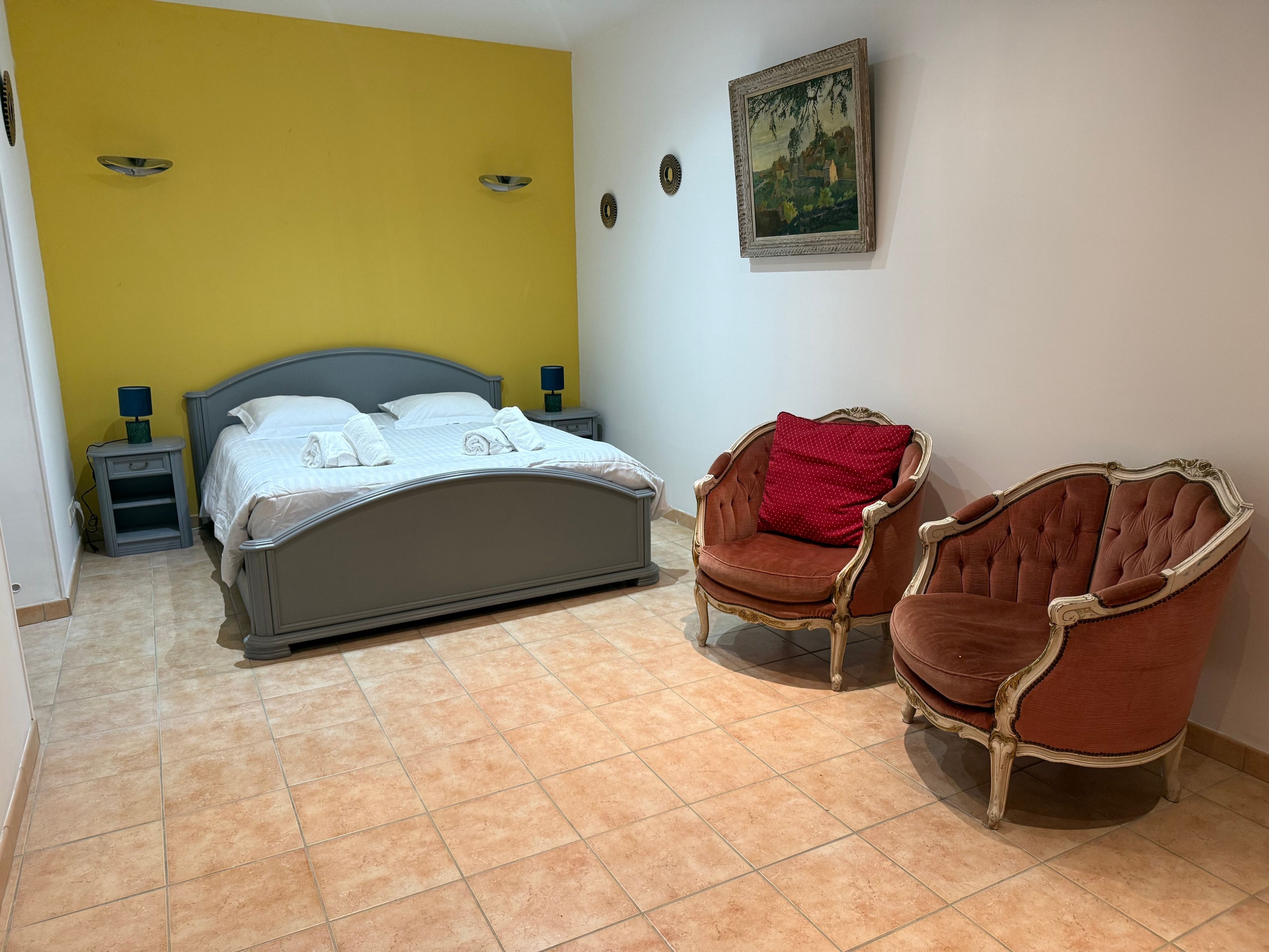 Une chambre à coucher avec un lit, deux tables de chevet, une chaise et un tableau au mur.