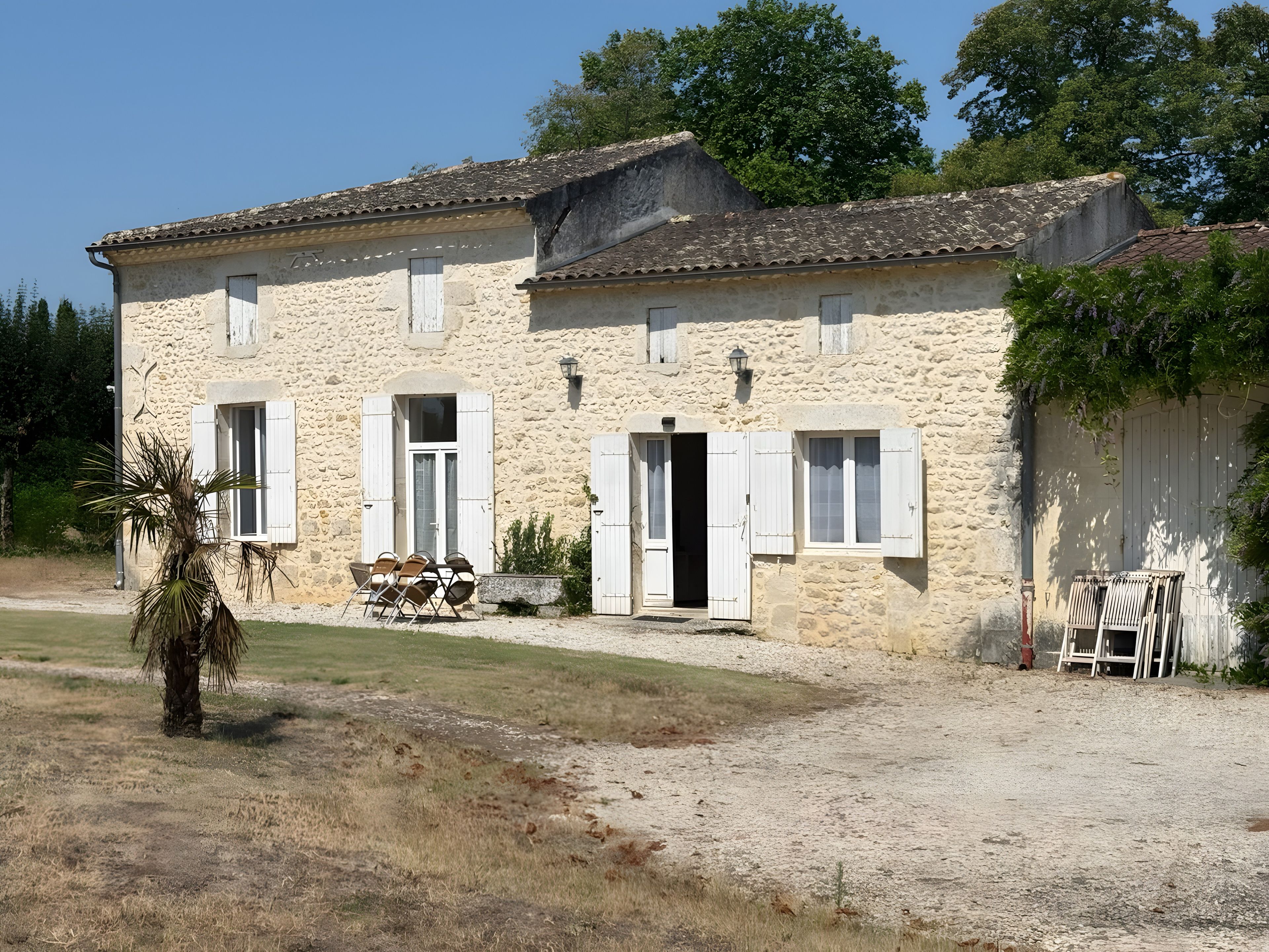 Un bâtiment en pierre avec une porte d’entrée, des fenêtres et un petit espace extérieur aménagé pour s’asseoir.