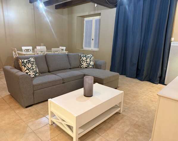 Una sala moderna con un sofá gris, una mesa de centro blanca y una ventana con cortinas.
