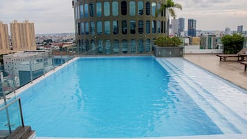 A rooftop swimming pool with a glass barrier and a cityscape view.