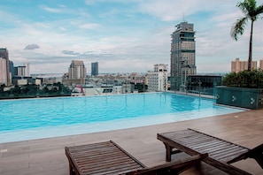 A rooftop pool with wooden loungers and a cityscape view. - Millennial360 Serviced Apartment (Phnom Penh)