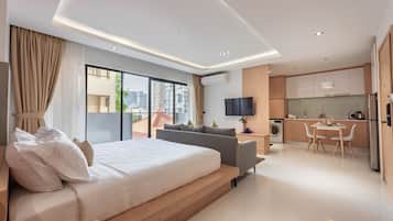 A modern hotel room with a large bed, a sofa, a dining area, and a kitchen.