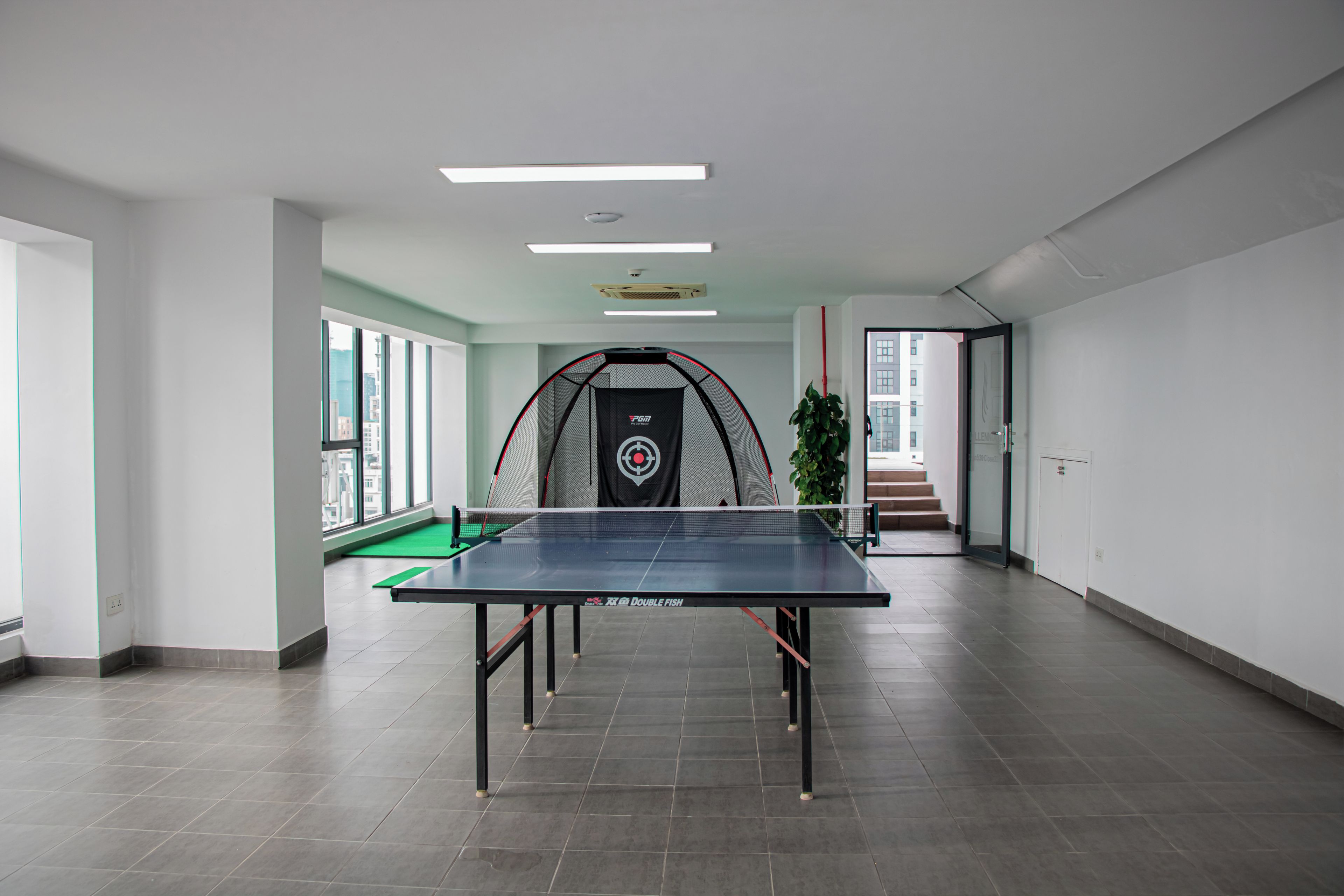 A spacious indoor area with a ping pong table, a netted enclosure, and a staircase leading to an outdoor area.