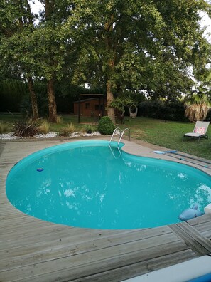 Piscina com deck de madeira, rodeada por árvores e uma rede.