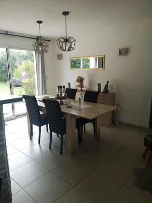 Uma sala de jantar com mesa de madeira, cadeiras pretas, luminária pendente e vista para o verde lá fora.