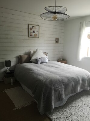 Quarto com cama, mesa de cabeceira, luminária, lustre e janela com cortinas.