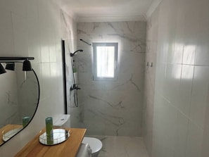 A bathroom with a marble wall, a wooden vanity, a toilet, a shower, and a window. - New Listing (Alcocéber)