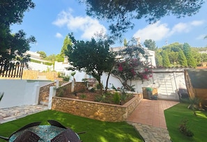 A garden with a stone planter, a white wall, and a tree with pink flowers. - New Listing (Alcocéber)
