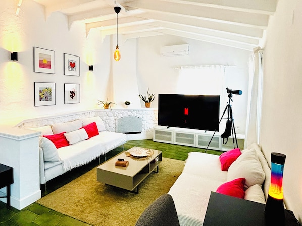 A living room with a white sofa, a coffee table, a flat-screen TV, and a tripod.