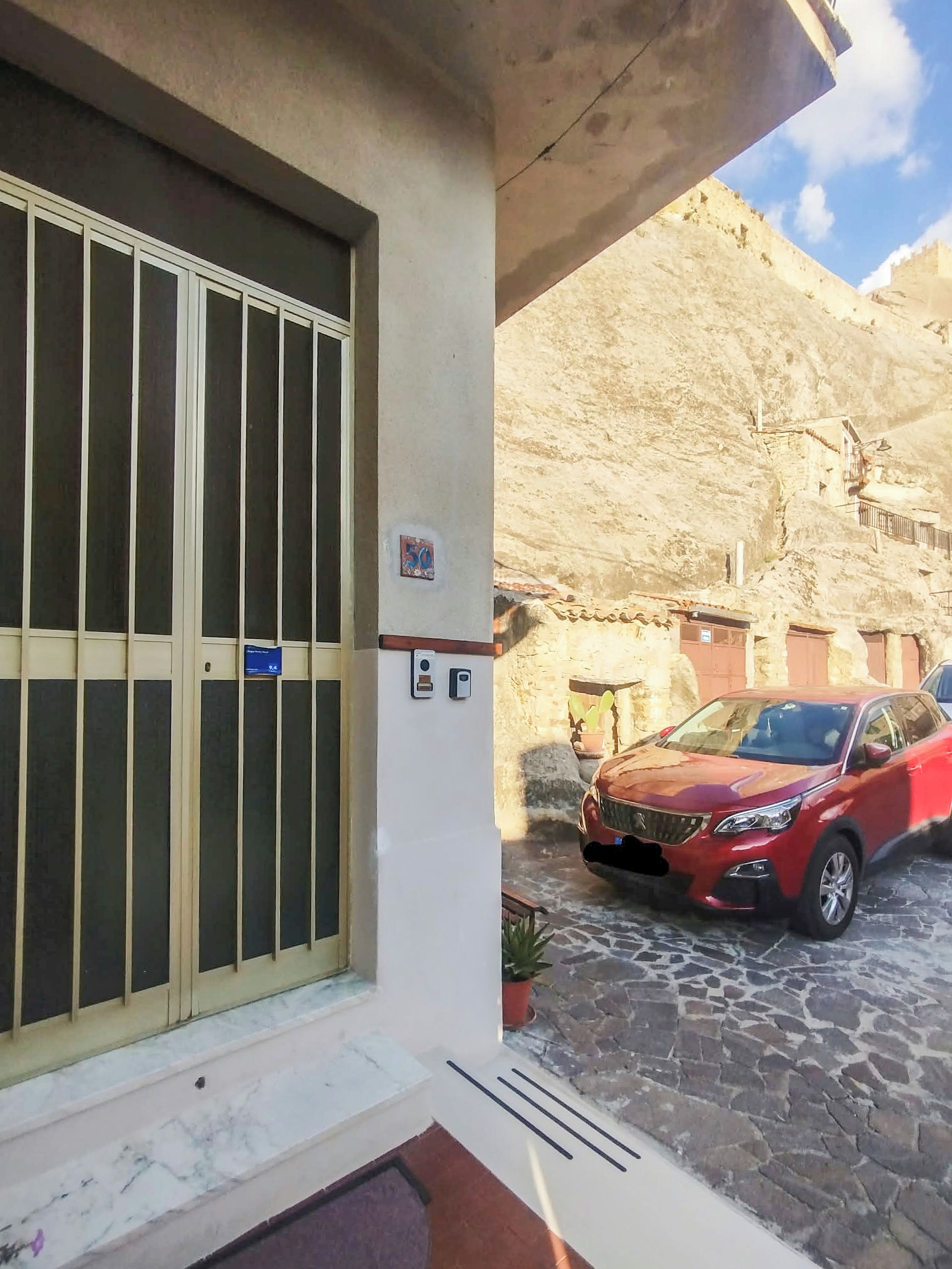 Entrada de um edifício com uma grande janela, uma porta e área de estacionamento com um carro vermelho.