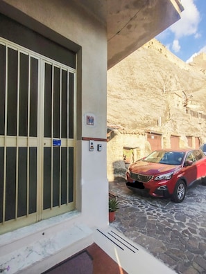 Entrada d'un edifici amb un gran finestral, una porta i una zona d'aparcament on hi ha un cotxe vermell.