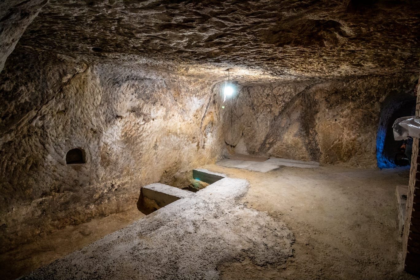 Eine Höhle mit Steinsitzbank, einer kleinen Nische und einer Lichtquelle.