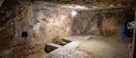 A cave interior with a stone bench, a small alcove, and a light source.