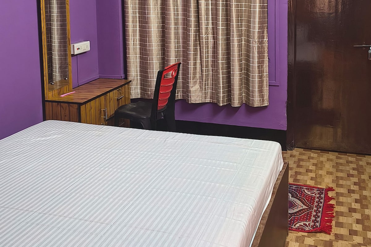 A room with a bed, a chair, a mirror, and a door.