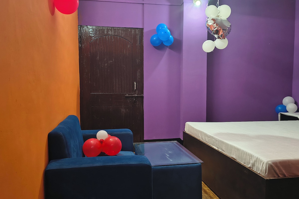 A room with a bed, a blue armchair, a small table, and purple walls.