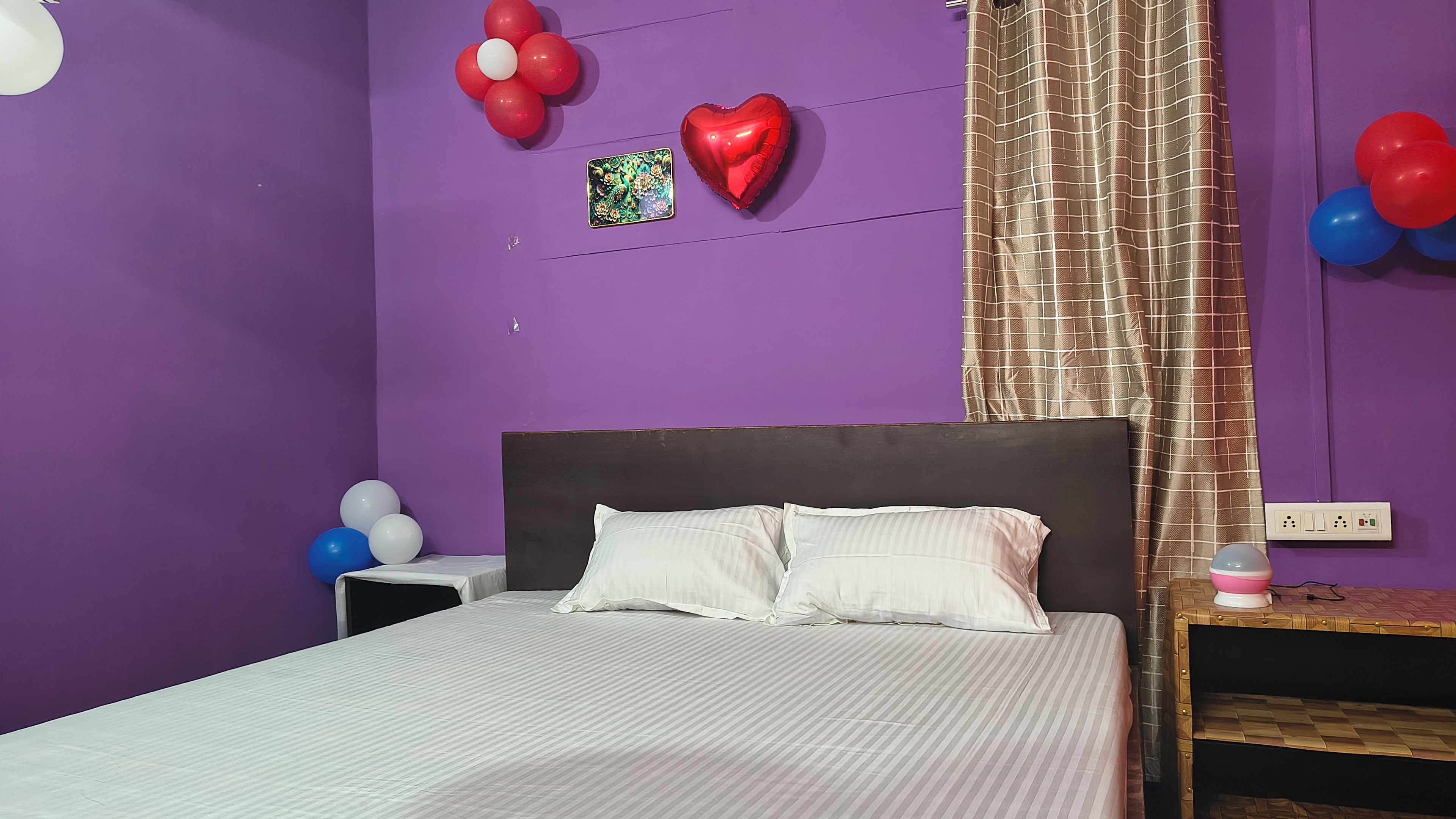 A room with a bed, a nightstand, and a wall with balloons.