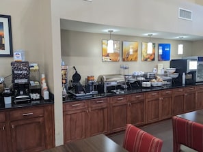 Um balcão de pequeno-almoço com máquinas de café, uma máquina de café Wake Up e várias opções de comida.