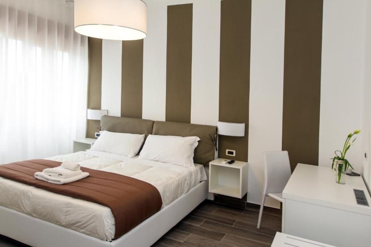 A hotel room with a bed, bedside tables, a desk, and a chair.