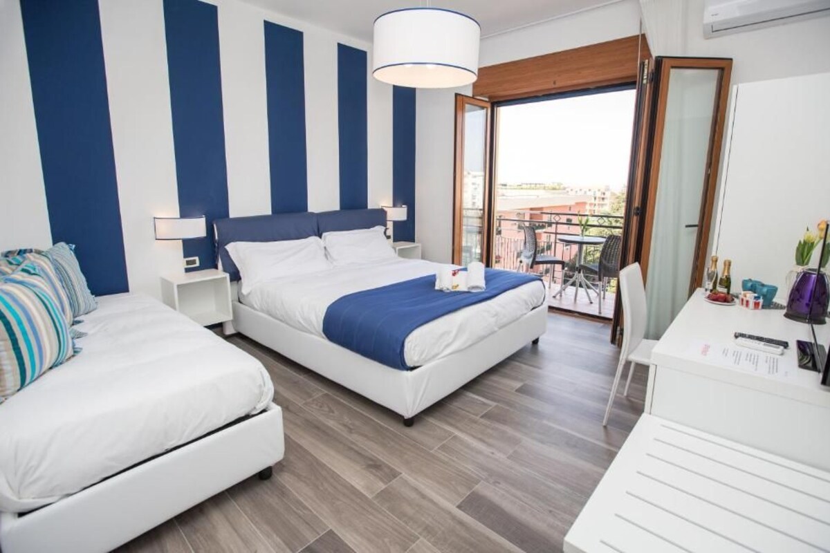 A hotel room with a bed, a desk, and a balcony with a view.