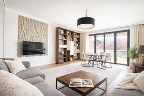 Un salon moderne comprenant un canapé, une table basse, un téléviseur, une bibliothèque, une table à manger, des chaises et une grande fenêtre offrant une belle vue.