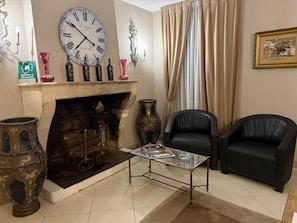 A room with a fireplace, two black leather chairs, a table with a magazine, and a large wall clock. - Country House 'Domaine Rollan De By' with Private Terrace, Wi-Fi and Air Conditioning (Bégadan)
