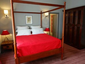 Cama de dossel com lençóis brancos, duas luminárias de cabeceira e uma impressão botânica emoldurada na parede.