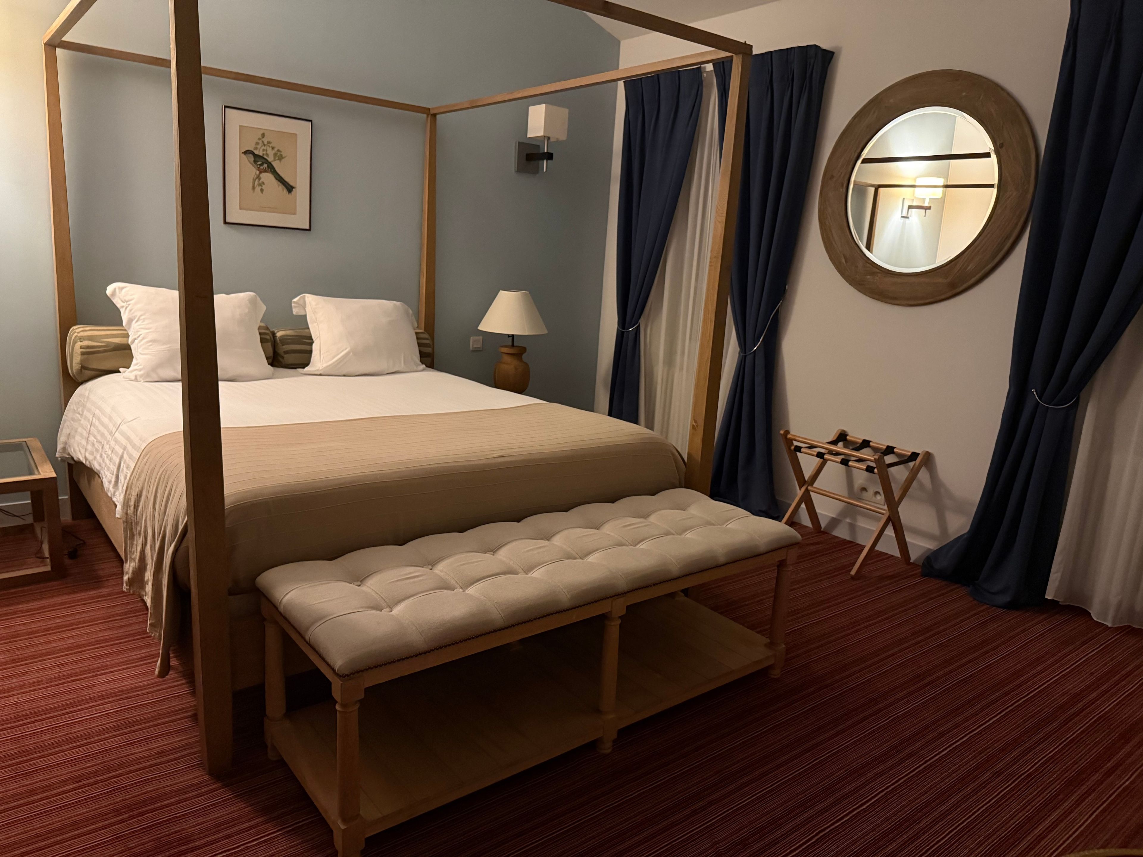 A four-poster bed with a bench, a bedside table, a lamp, and a framed picture on the wall.