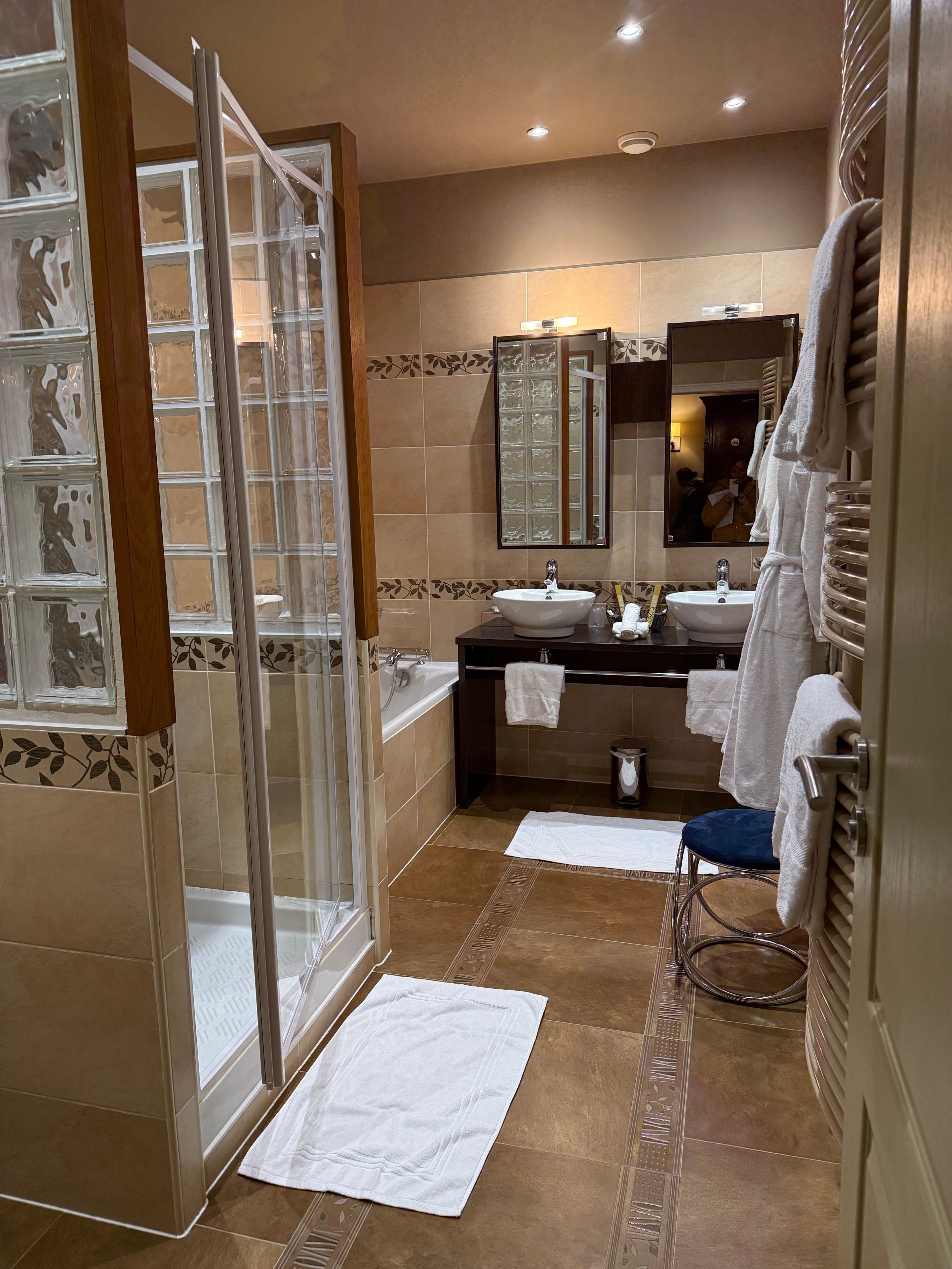 A modern bathroom with a glass shower enclosure, two sinks, a large mirror, and a towel rack.
