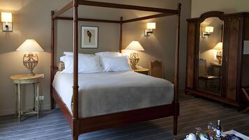 A four-poster bed with white linens, two bedside lamps, a framed picture on the wall, and a wooden wardrobe with a mirror.