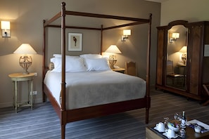 Uma cama com dossel com lençóis brancos, duas luminárias de cabeceira, um quadro na parede e um guarda-roupa de madeira com espelho.