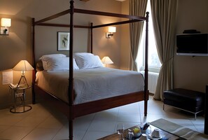 A four-poster bed with white linens, a bedside table with a lamp, a framed picture on the wall, and a television on the wall. - Country House 'Domaine Rollan De By' with Private Terrace, Wi-Fi and Air Conditioning (Bégadan)