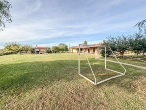 A grassy field with a metal structure, possibly a goalpost, and a building with a red roof in the background. - Casal del Falco - Surrounded by Nature (Tarquinia)