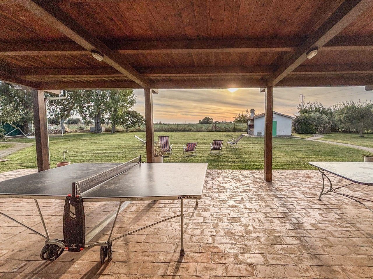 An outdoor ping pong table set up on a brick patio with a covered area overhead.