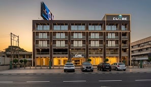 A multi-story commercial building with a prominent 'CUBE' sign, multiple balconies, and a parking area with several cars.
