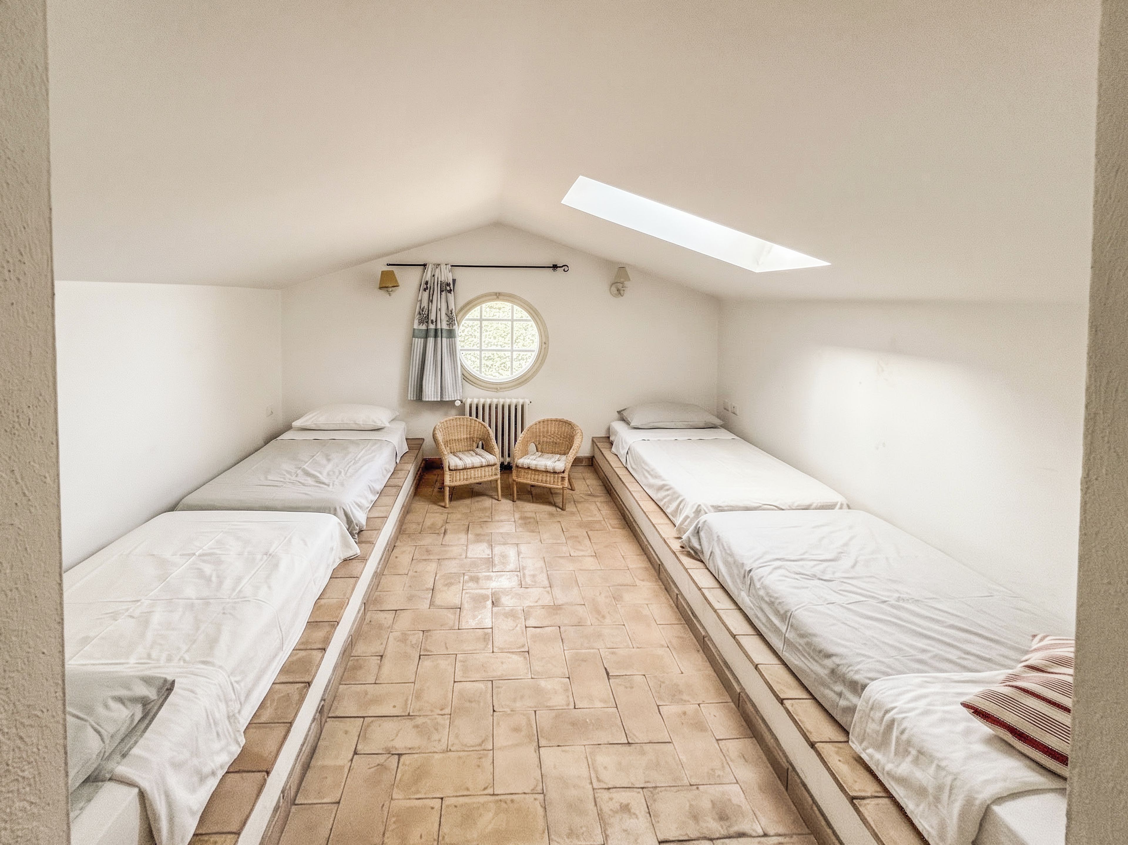 Ein Schlafsaalzimmer mit zwei Einzelbetten, einem Rundfenster, einer Heizung und einem Dachfenster.