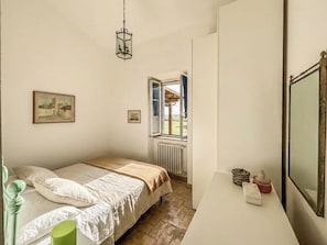 A bedroom with a bed, a window, a radiator, and a bedside table with decorative items. - Casal del Falco (Lazio)
