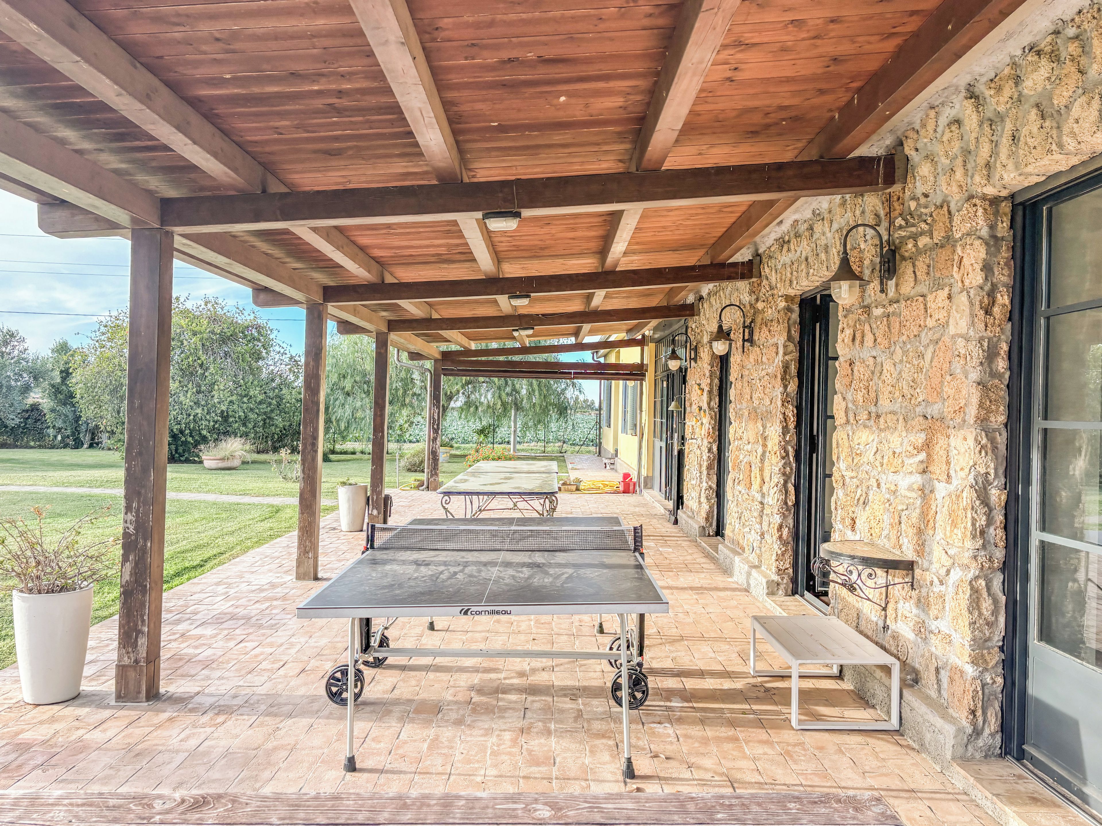 Un patio al aire libre con mesa de ping pong, paredes de piedra y techo de madera.