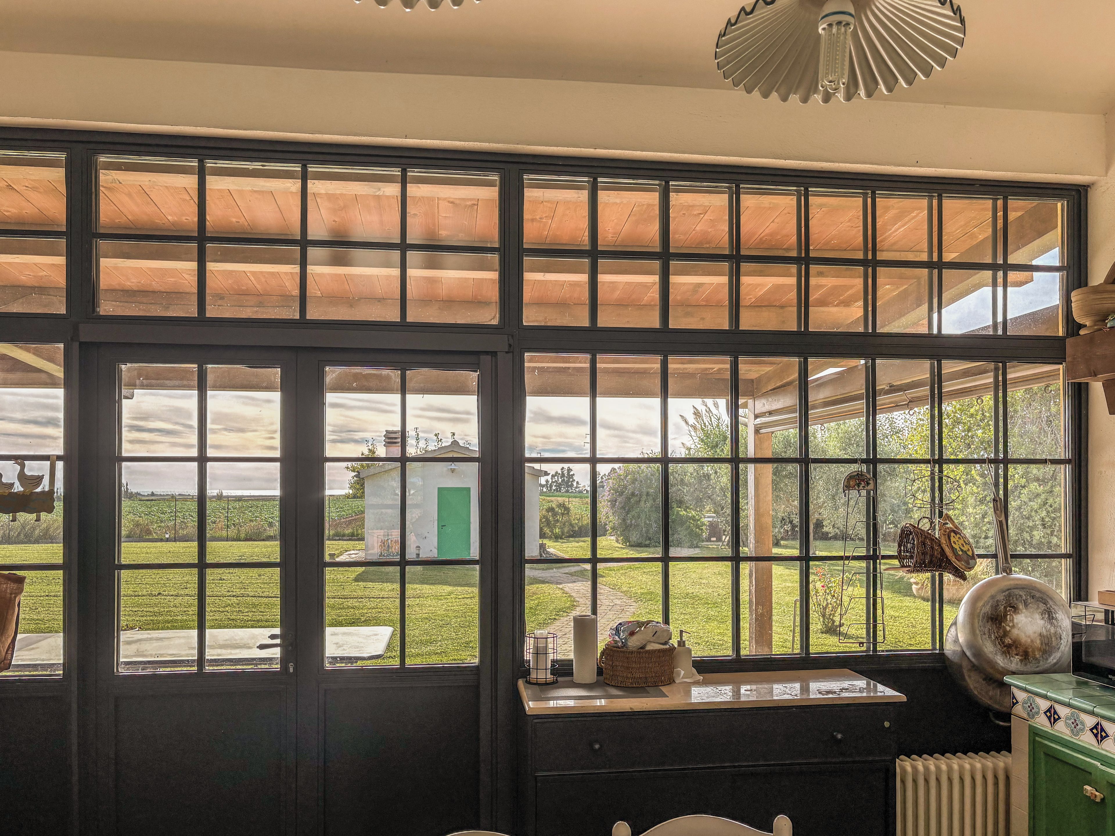 Una stanza con ampie finestre, un soffitto in legno e vista su un paesaggio verde.