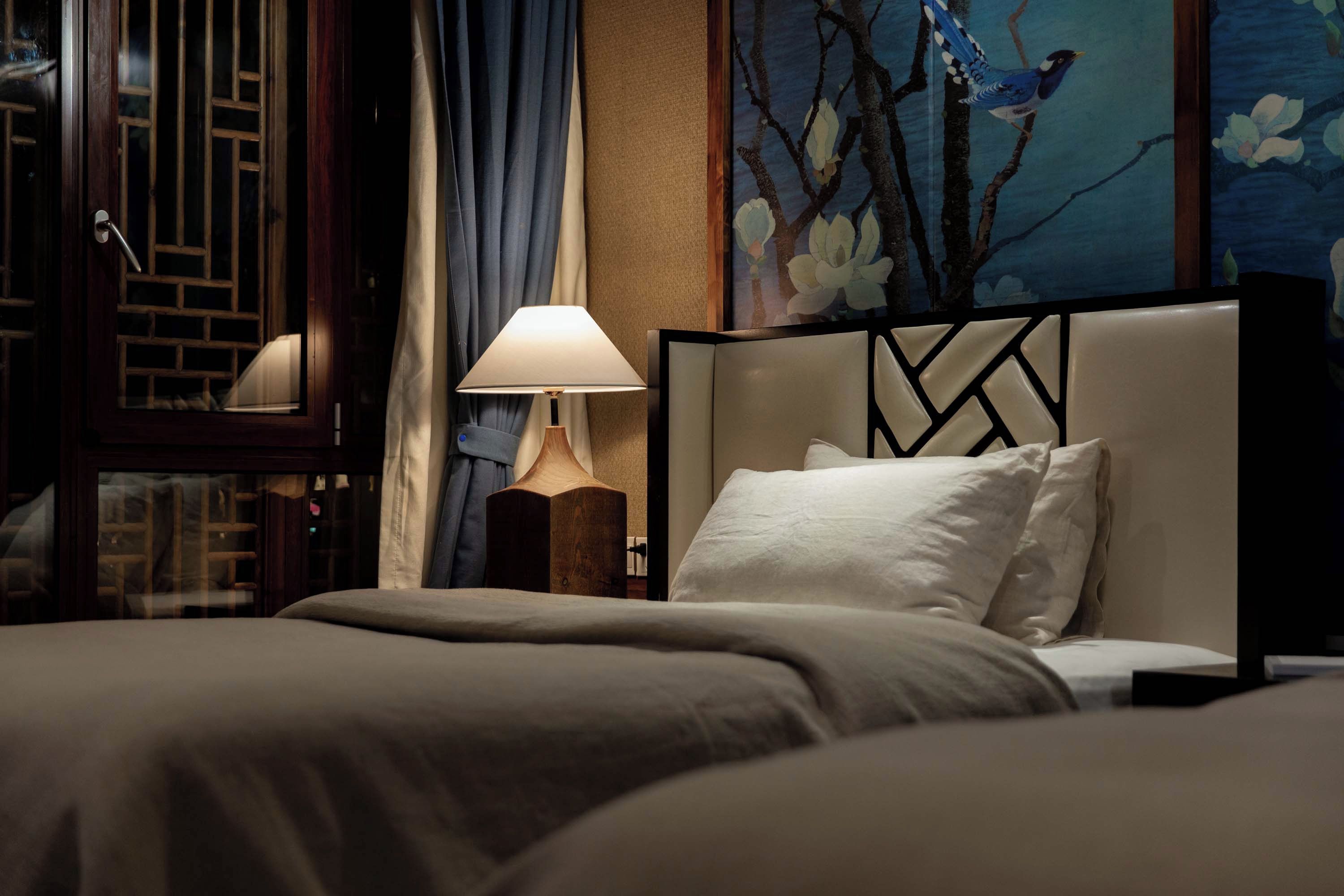 A hotel room with a bed, a lamp, and a painting of a bird on the wall.