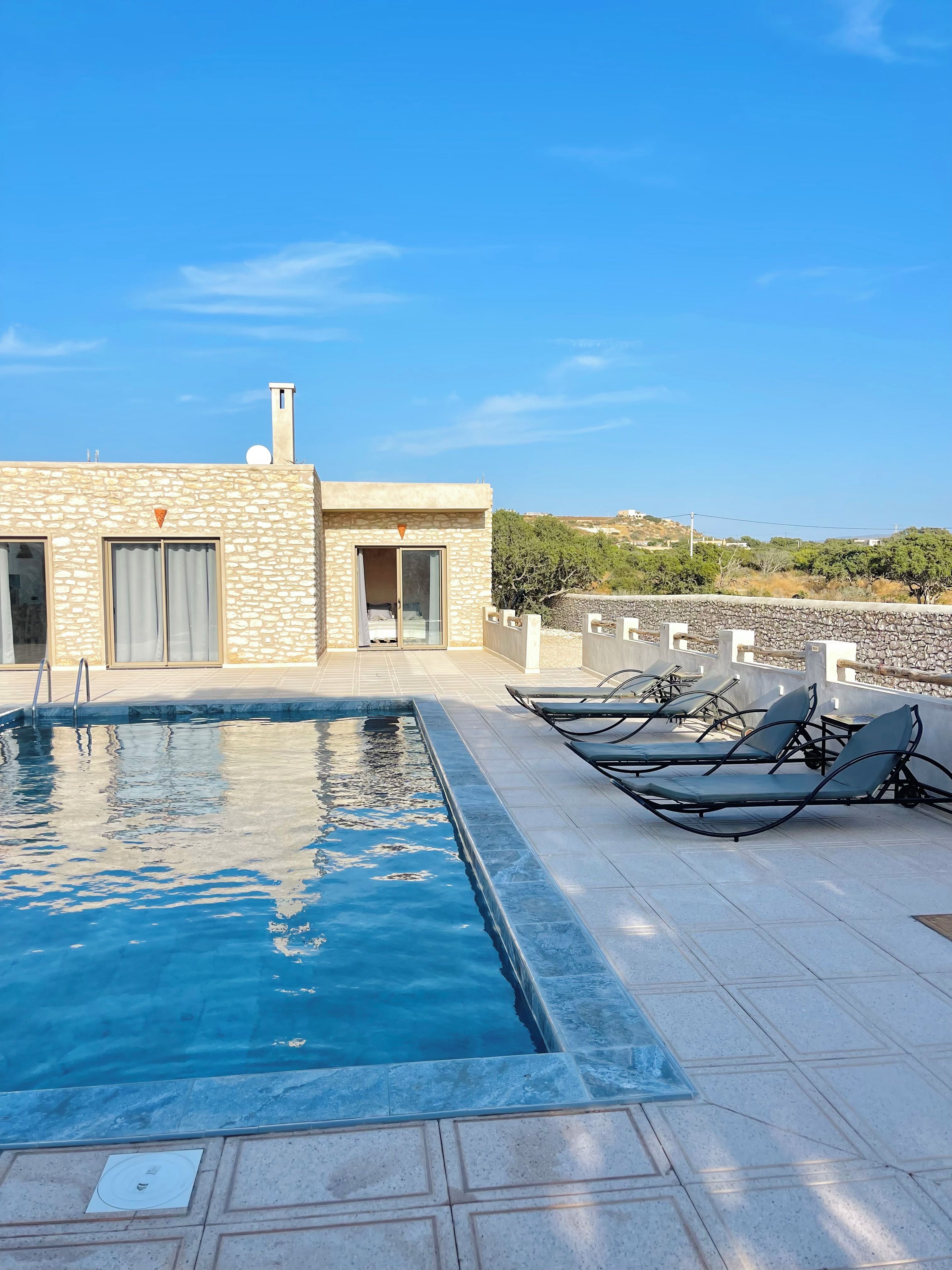 Un espace piscine aménagé sur le toit, avec un bâtiment en pierre, une porte et des chaises longues.