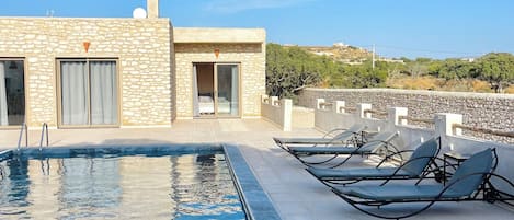 A rooftop pool area with a stone building, a door, and lounge chairs.