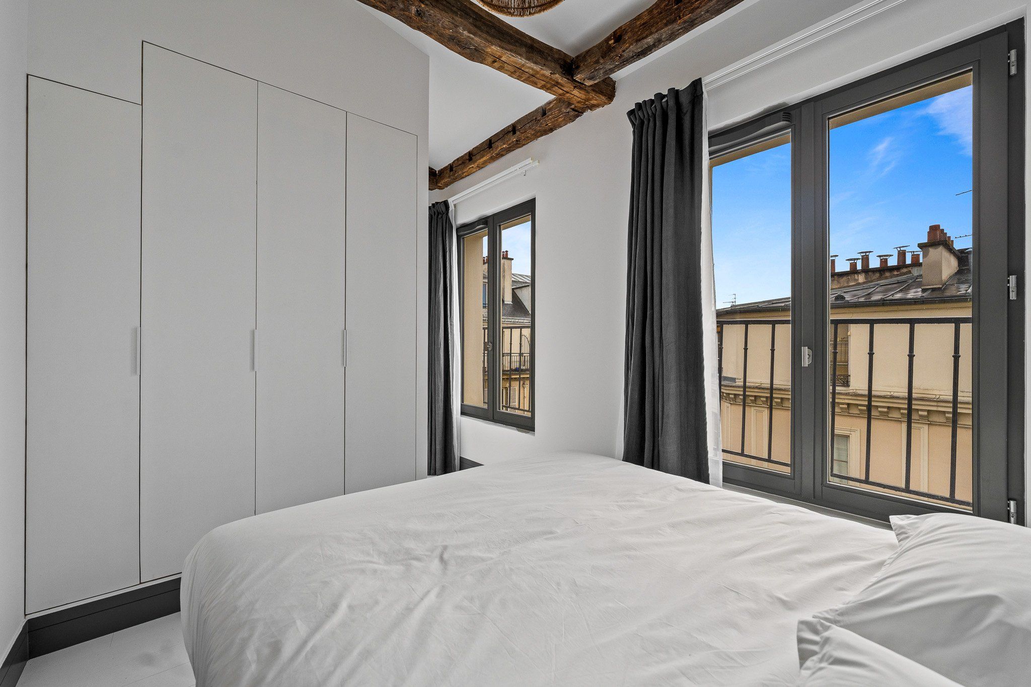 A bedroom with a large bed, a wardrobe, and a window with a view of buildings.