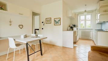 Una cocina moderna con armarios blancos, un comedor con mesa y sillas blancas, y una sala de estar con sofá marrón.
