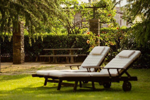 A garden with a stone pillar, a wooden bench, and two sun loungers.